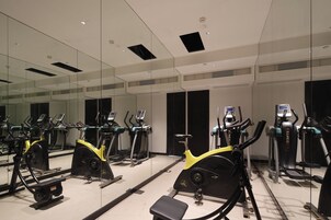 Un gimnasio con varias máquinas de ejercicio y un amplio ventanal con espejos.