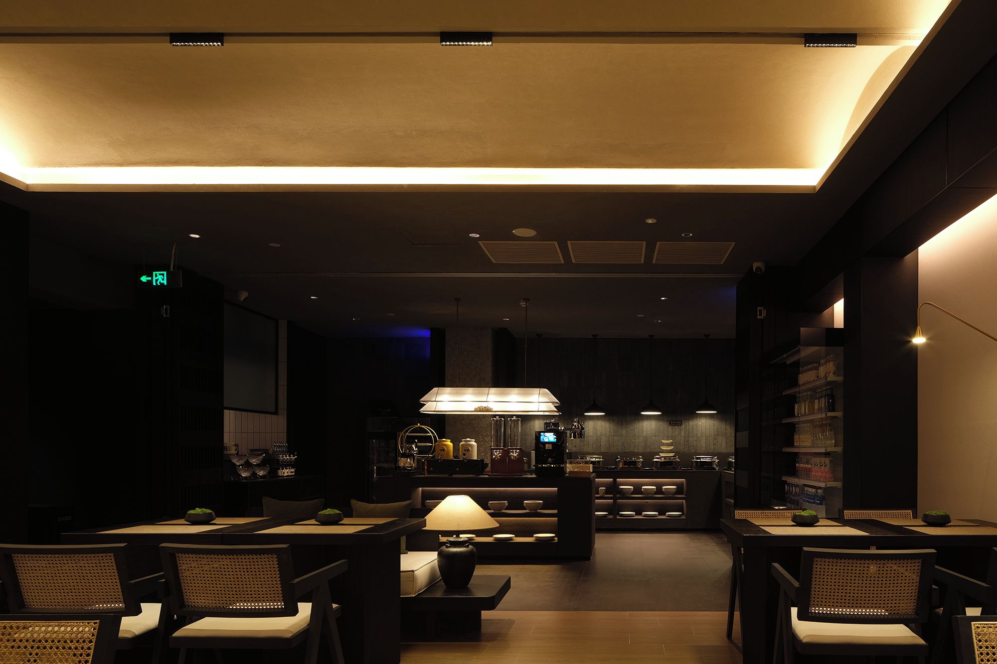 Un restaurante tenuemente iluminado con una zona de comedor central, un bar y una cocina al fondo.