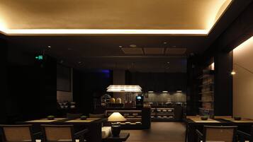 Un restaurante tenuemente iluminado con una zona de comedor central, un bar y una cocina al fondo.
