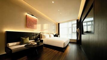 A modern hotel room with a large bed, a sofa, a small table, and a large window.