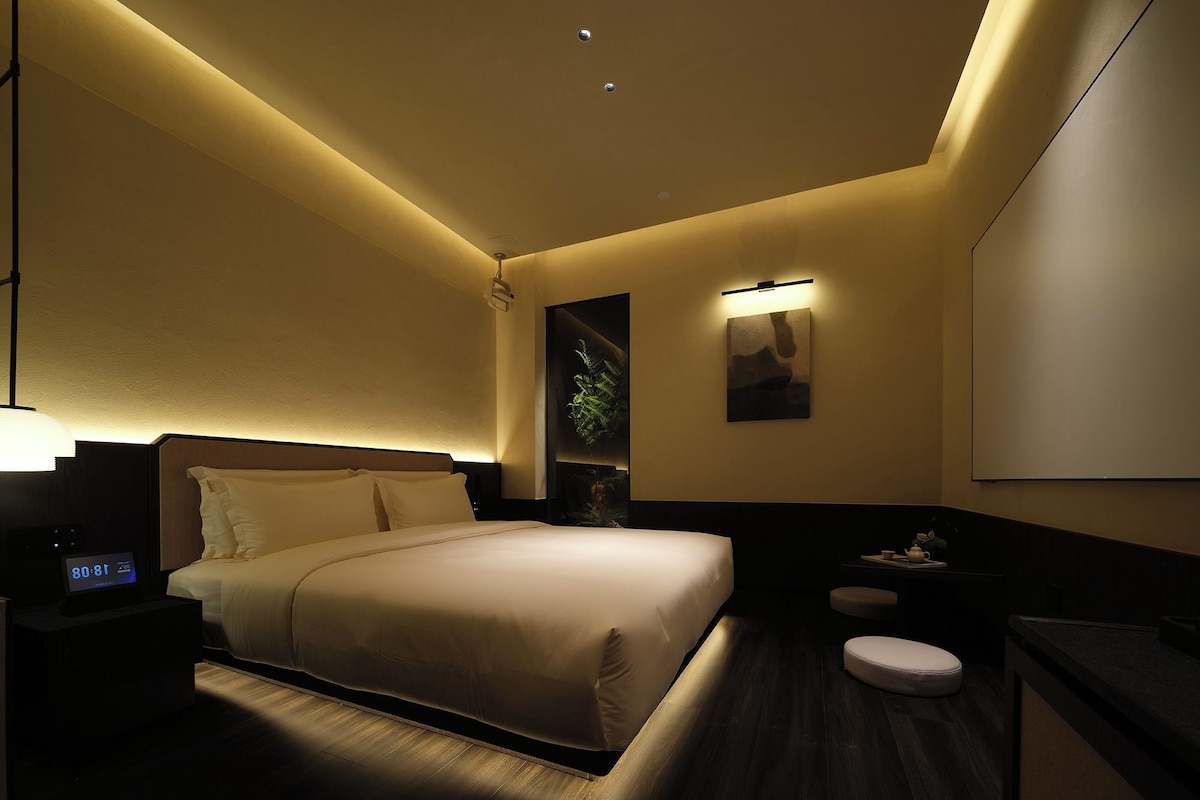 A hotel room with a bed, bedside table, nightstand, and a wall-mounted TV.