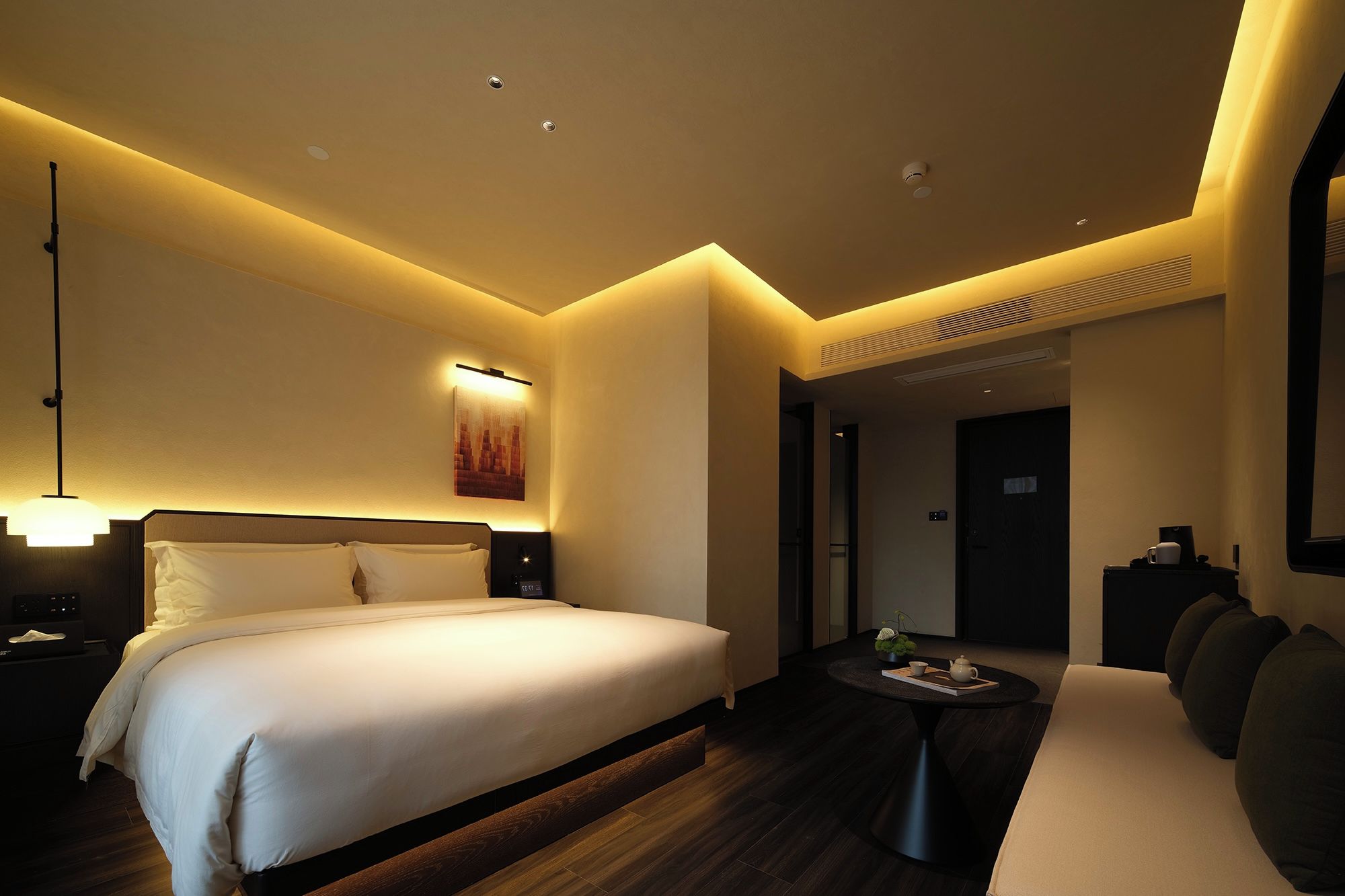 A hotel room with a large bed, bedside table, and a small seating area with a table and chairs.