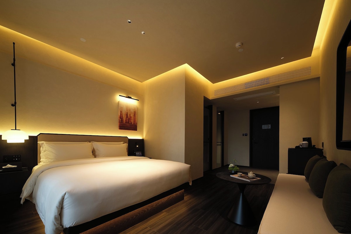 A hotel room with a large bed, bedside table, and a small seating area with a table and chairs.
