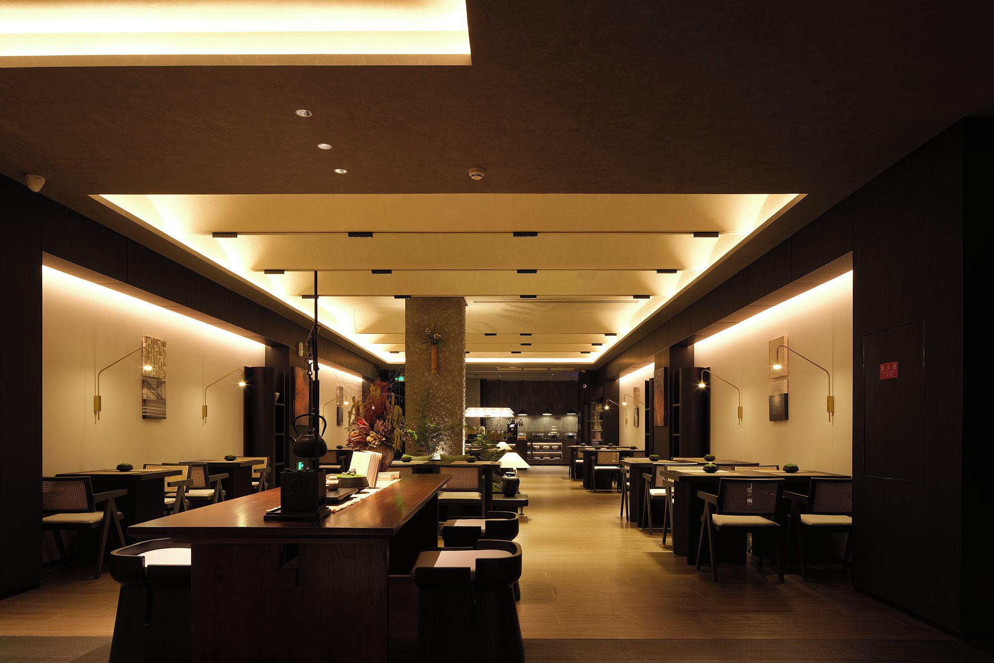 A modern interior with a long dining area, multiple tables, and chairs, and a central pillar.
