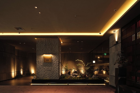 A modern lobby with a stone pillar, recessed lighting, and indoor plants. - YOMANJO (Guangzhou)