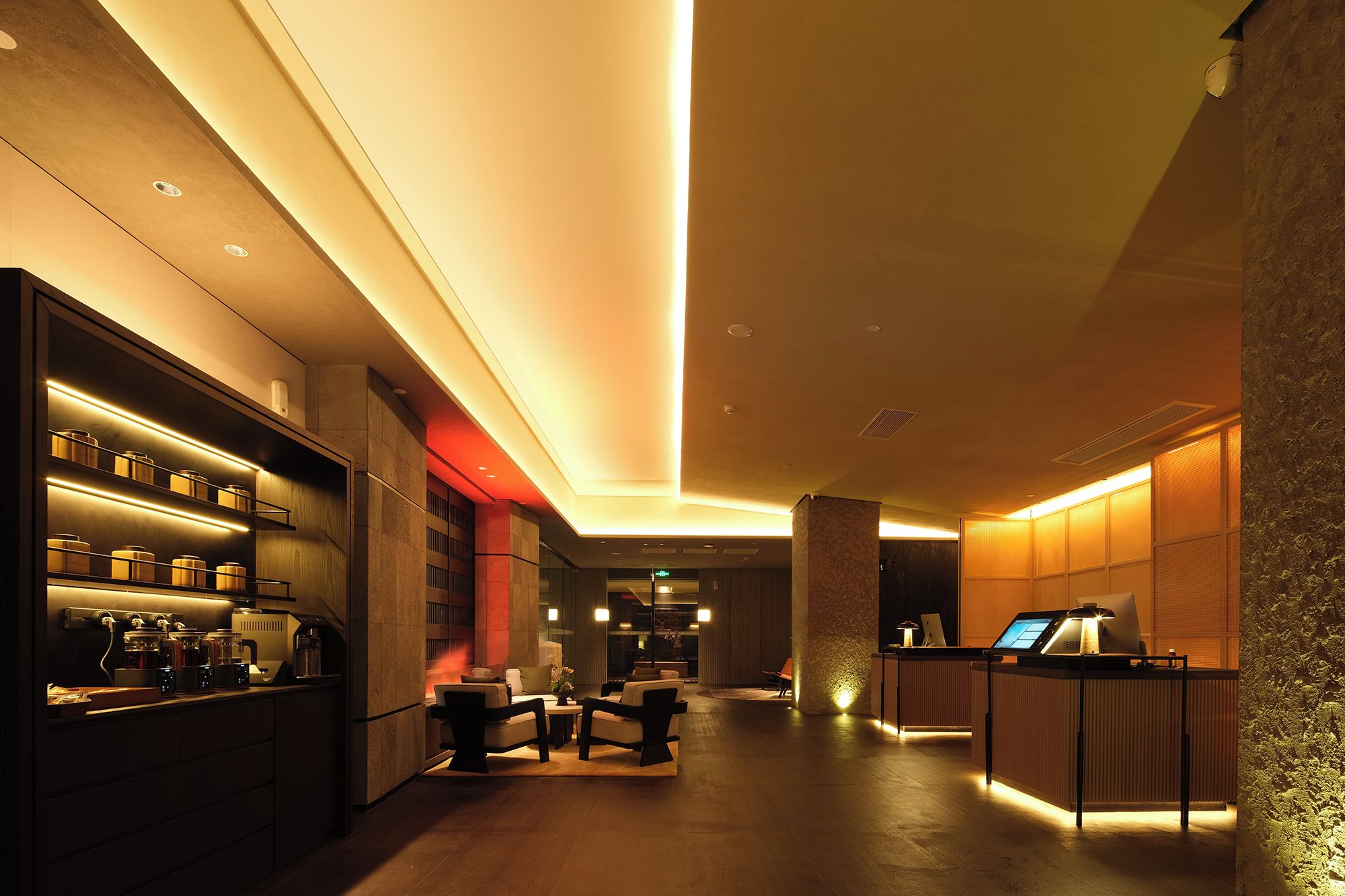 A modern hotel lobby with a reception desk, seating area, and a bar with illuminated shelves.