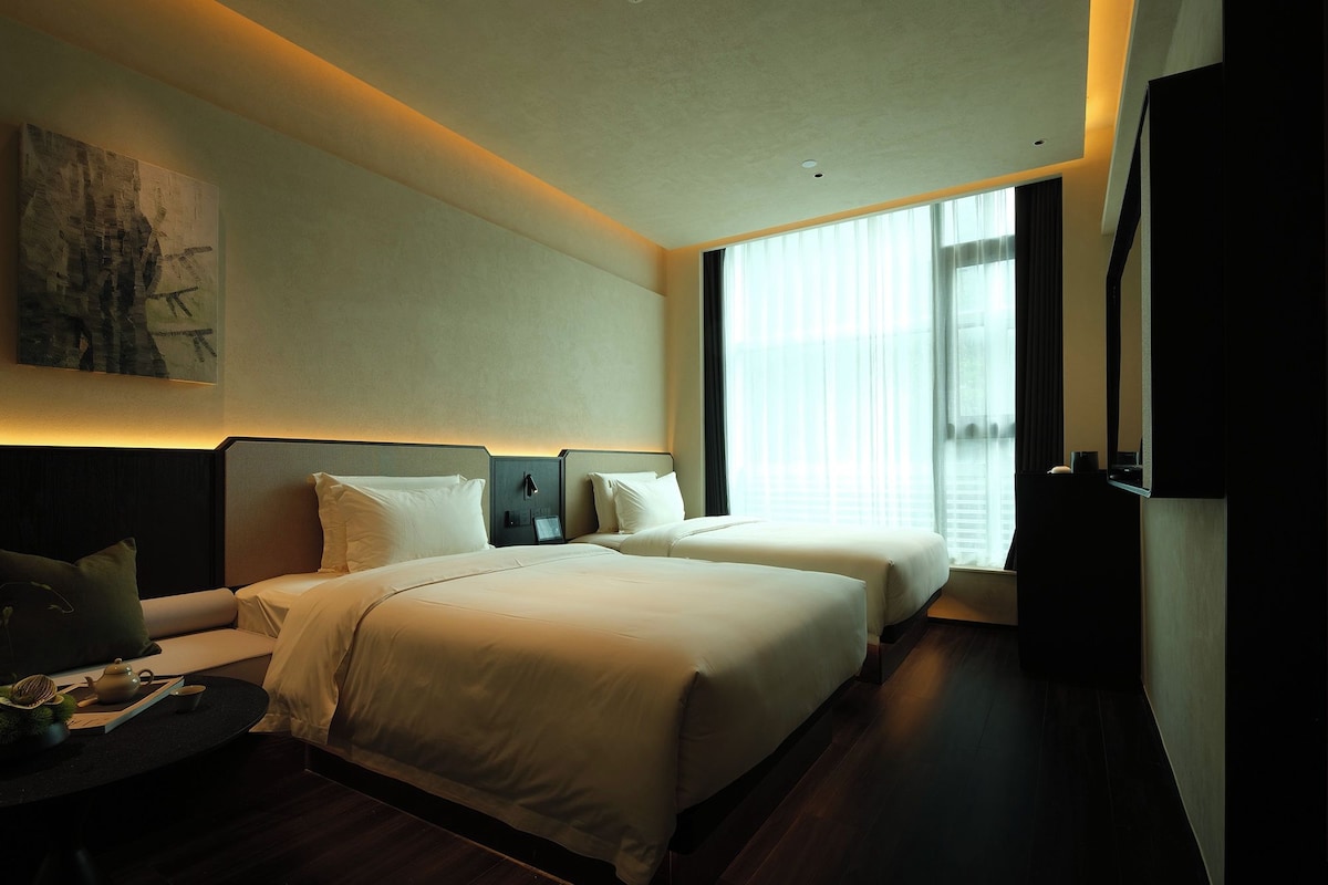 A hotel room with a large bed, a bedside table, a TV, and a window with curtains.