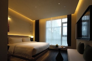 A hotel room with a bed, bedside table, and a TV. - YOMANJO (Guangzhou)