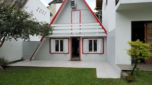 Une maison avec un toit à forte pente, des murs extérieurs blancs et des volets rouges.