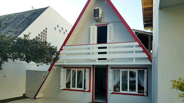 Een tweelaags huis met een rode en witte buitenkant, een balkon en een klein raam.