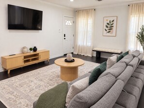 Un saló modern amb un sofà gris, una taula de centre de fusta, una televisió i una decoració minimalista.
