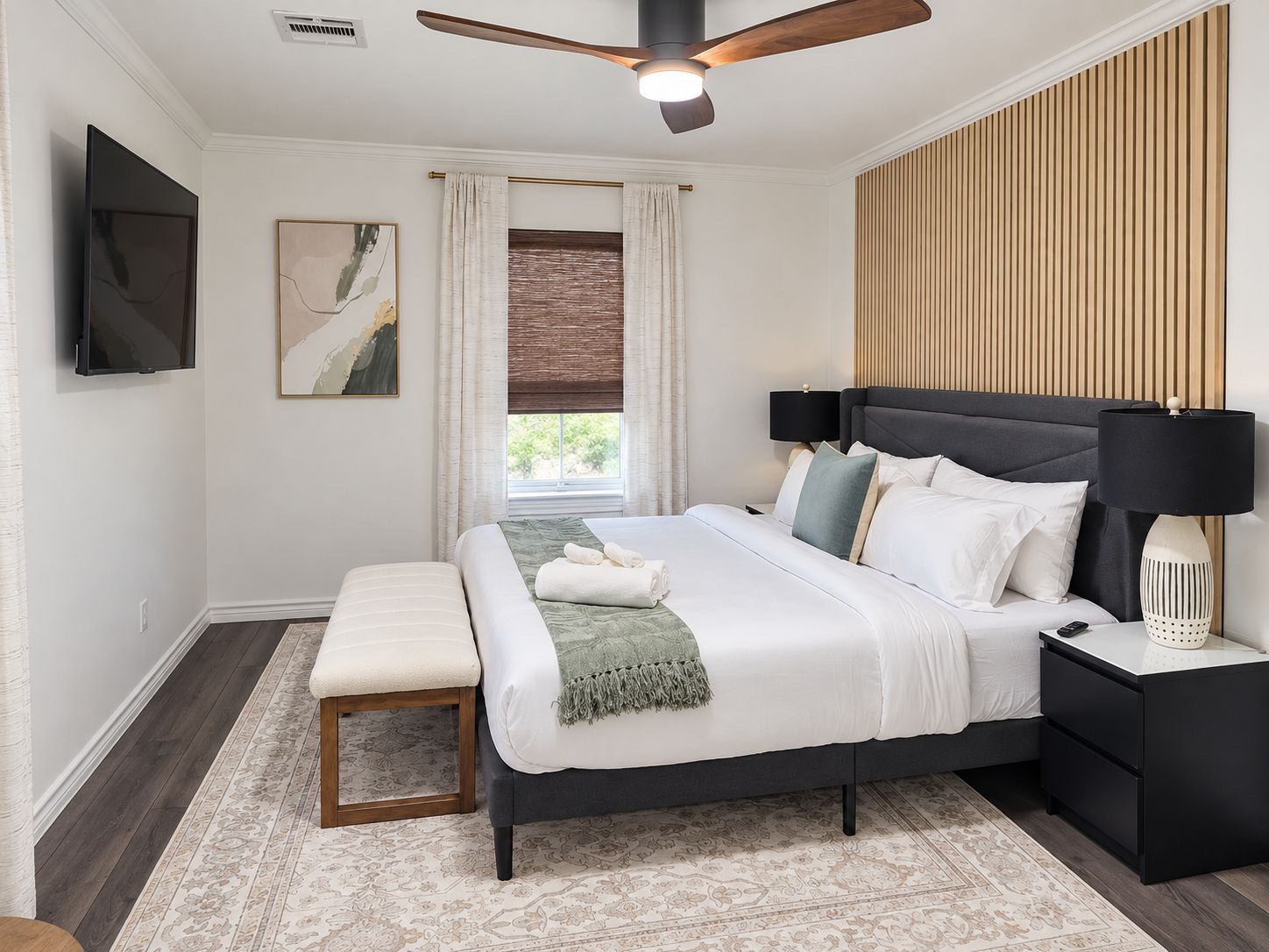 A modern bedroom with a bed, bedside tables, a ceiling fan, a TV, and a window with curtains.