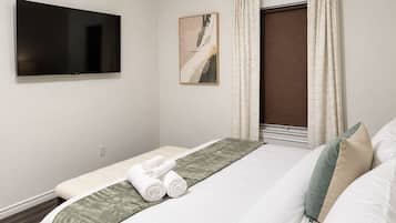 Una habitación de hotel con cama, televisor de pantalla plana en la pared, un cuadro y una ventana con cortinas.
