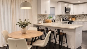 Una cocina moderna con armarios blancos, una isla central con taburetes y una zona de comedor con mesa redonda y sillas.