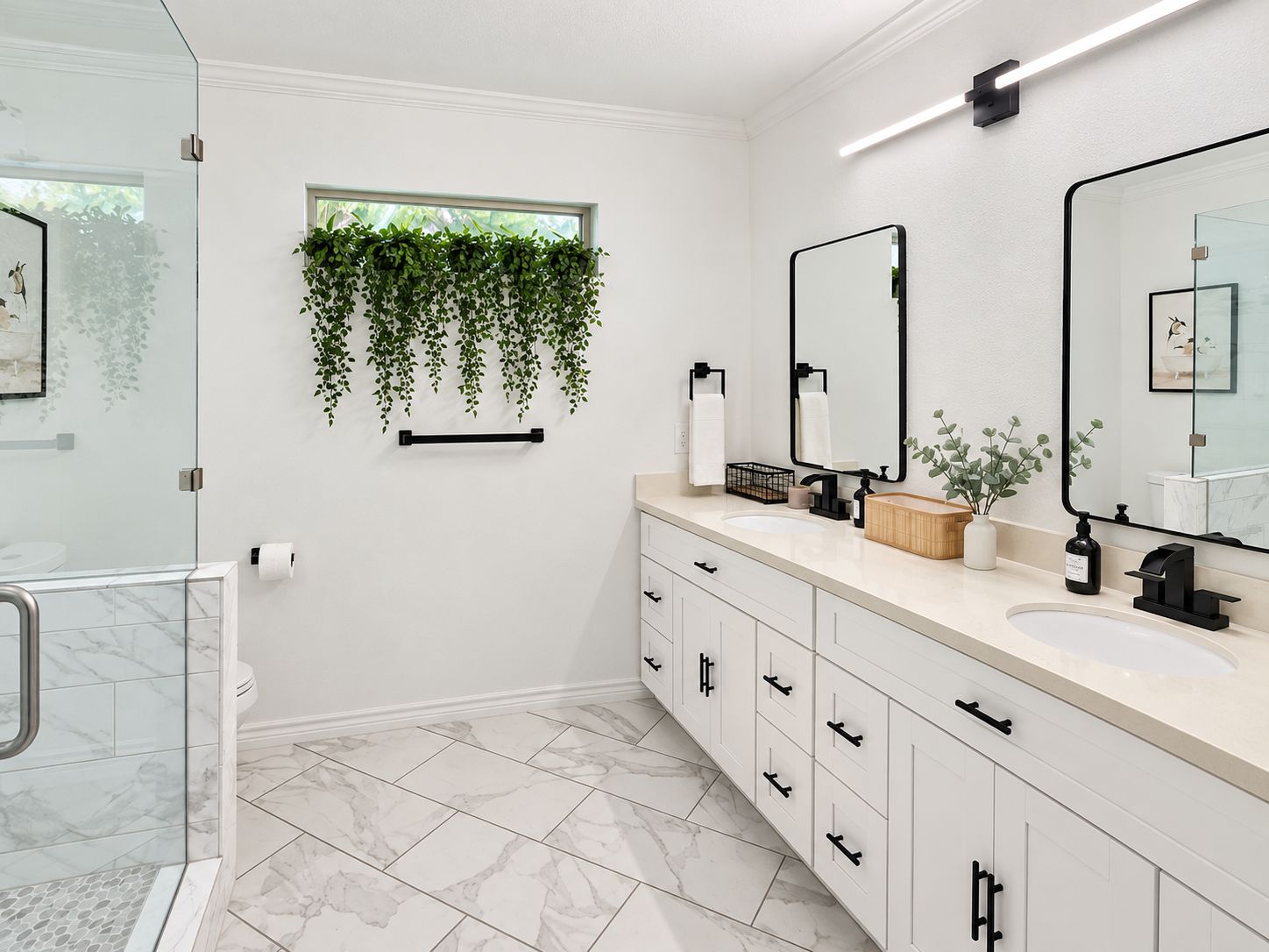 A modern bathroom with a glass shower enclosure, a large mirror, and a window with hanging plants.