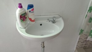Valkoinen pesuallas, jossa on krominen hana, kaksi pulloa henkilökohtaisen hygienian tuotteita ja laatoitettu seinä.