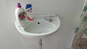 A white sink with a chrome faucet, two bottles of personal care products, and a tiled wall. - Uni Inn Semarang Gunung Pati Akbid Abdi Husada (Semarang)