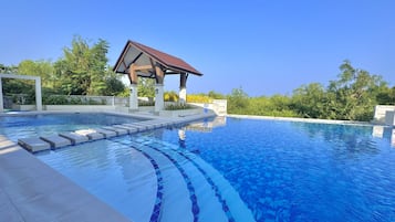 A swimming pool with a tiled edge, a covered pavilion, and surrounding greenery.