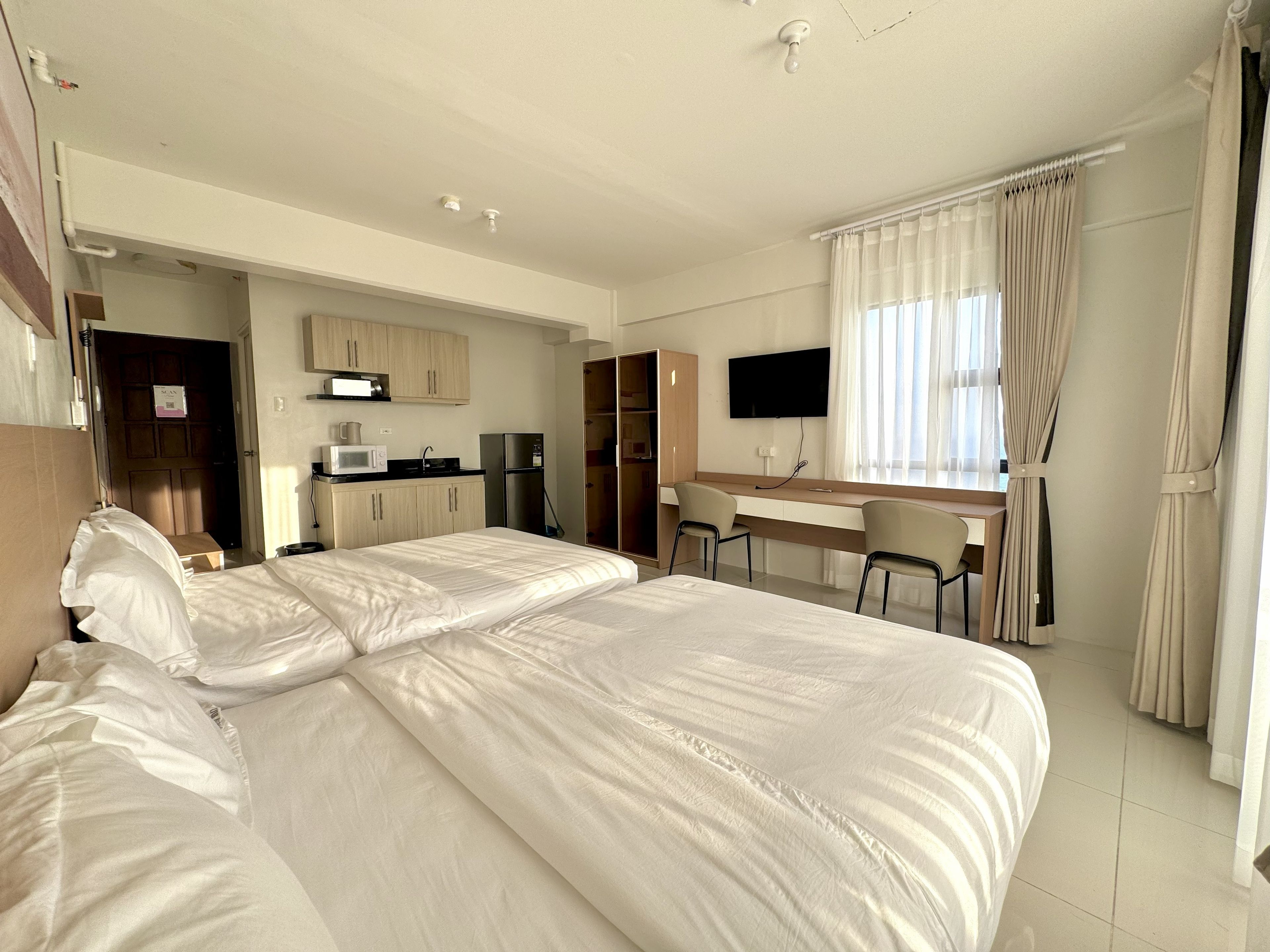 A hotel room with a bed, a desk, a TV, and a kitchenette.