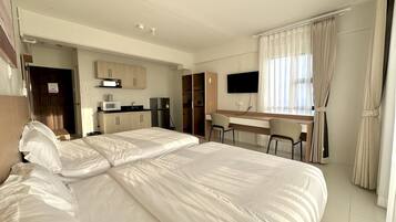 A hotel room with a bed, a desk, a TV, and a kitchenette.