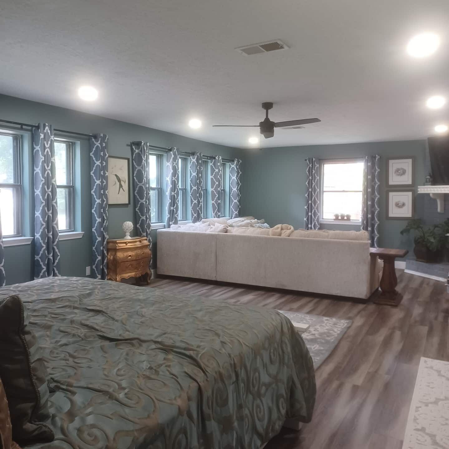 A bedroom with a bed, a sofa, a nightstand, and a ceiling fan.