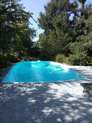 A swimming pool with a tiled deck, surrounded by trees and a building in the background. - Private 3-bedroom guest suite for up to 6 guests featuring a full kitchen, comfortable living space, private entrance, and swimming pool. Enjoy a peaceful, gated setting with convenient access to Conroe, The Woodlands, shopping, dining, hospitals (Conroe)