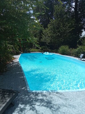 Una piscina rectangular con agua cristalina azul, rodeada de árboles y un solárium de hormigón.
