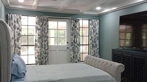 Ein Schlafzimmer mit einem großen Bett, einem Fernseher und einem Fenster mit Vorhängen.