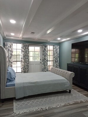 A bedroom with a large bed, a television, and a window with curtains. - Private 3-bedroom guest suite for up to 6 guests featuring a full kitchen, comfortable living space, private entrance, and swimming pool. Enjoy a peaceful, gated setting with convenient access to Conroe, The Woodlands, shopping, dining, hospitals (Conroe)