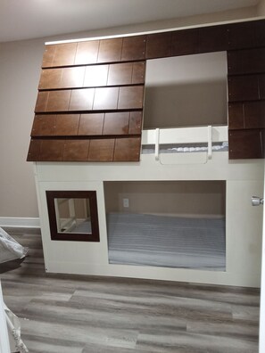 A bunk bed with a wooden headboard, a small window, and a white mattress.