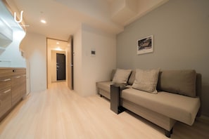 A modern hotel room with a sofa, a small table, and a kitchen area with cabinets. - unito residence SHINSAIBASHI East (Chuo-ku,)