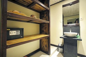 Une salle de bain avec une étagère en bois, un coffre-fort noir et un lavabo blanc.
