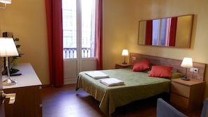 Une chambre d’hôtel comprenant un lit, deux tables de chevet avec des lampes, un bureau avec une lampe, une chaise et une fenêtre avec des rideaux.