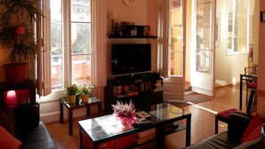 Un salon avec un téléviseur, des étagères à livres, une table basse et une plante en pot.