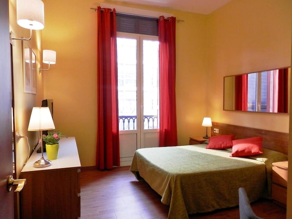 A hotel room with a bed, bedside tables, a desk, a chair, a potted plant, and a window with curtains. - Barcelona Central Garden (Barcelona)