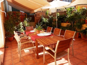 An outdoor patio with a wooden table and chairs, surrounded by potted plants and a thatched roof. - Barcelona Central Garden (Barcelona)