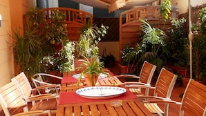 Une terrasse extérieure avec des tables et des chaises en bois, entourée de plantes en pot.