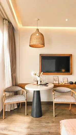 Uma sala de estar moderna com uma mesa redonda, duas poltronas estofadas, uma televisão de tela plana grande fixada na parede e um lustre.