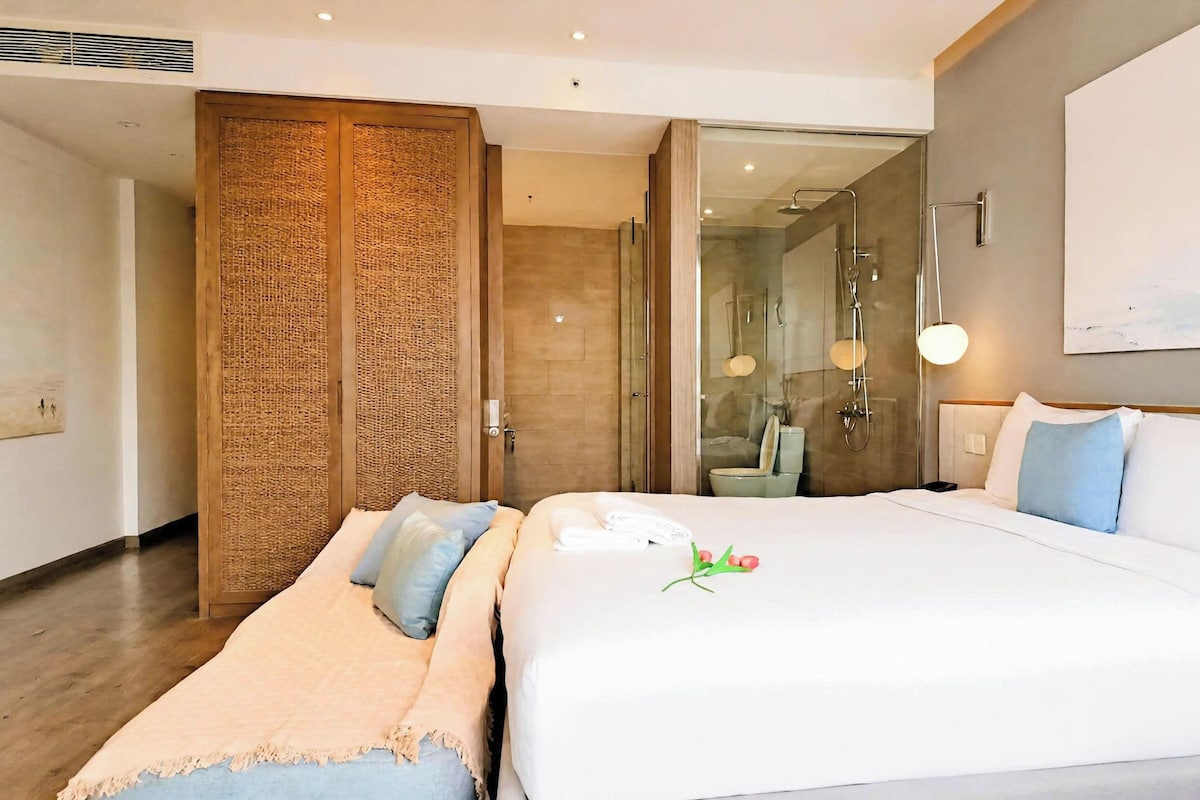 Quarto de hotel com cama, banheiro com chuveiro de vidro e armário de madeira.