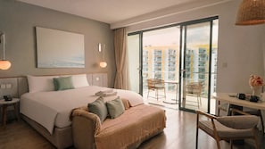 Quarto de hotel com uma cama grande, mesa de cabeceira com telefone, uma cadeira, varanda com mesa e cadeiras, e vista para a cidade.