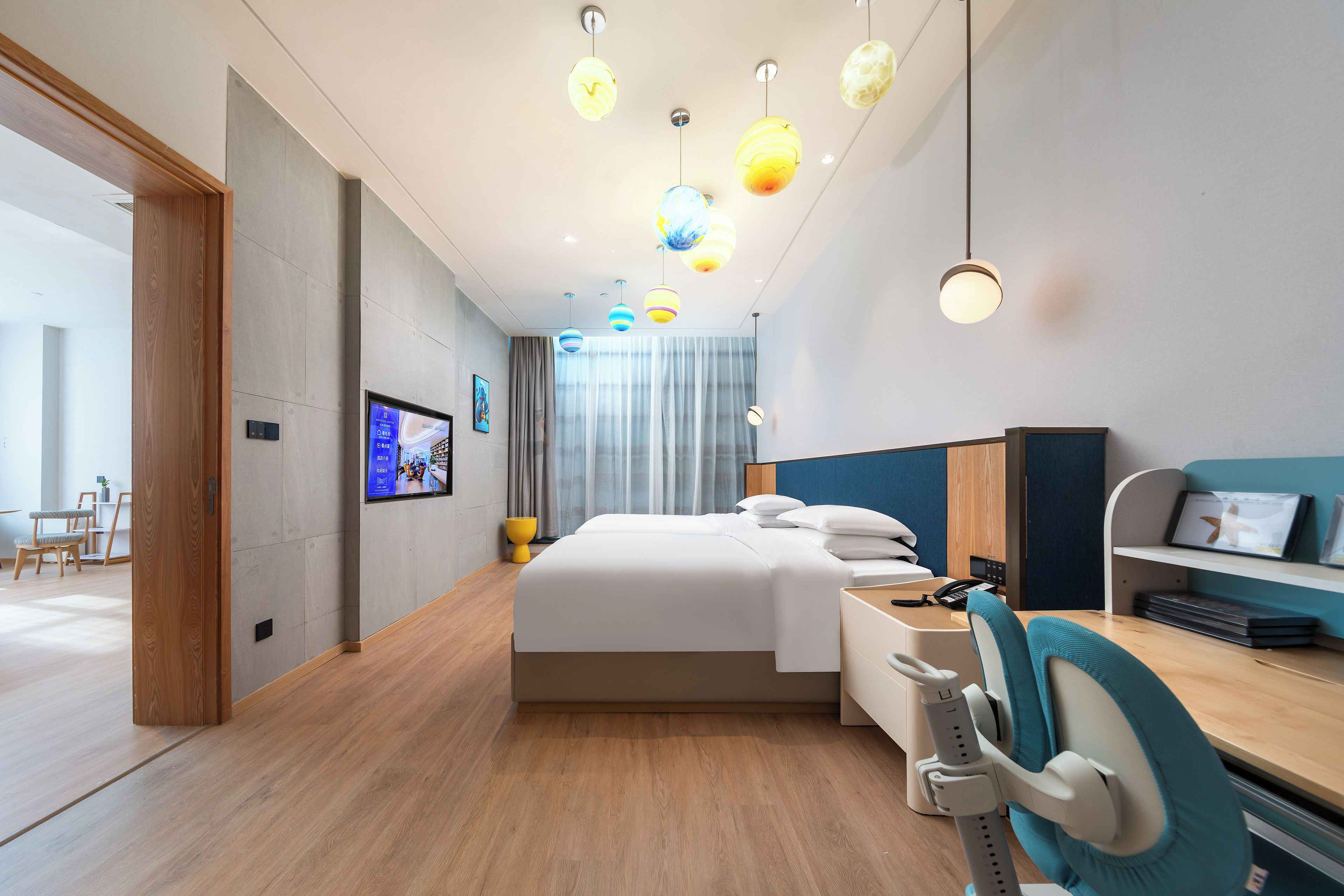 A modern hotel room with a bed, desk, chair, and a television on the wall.