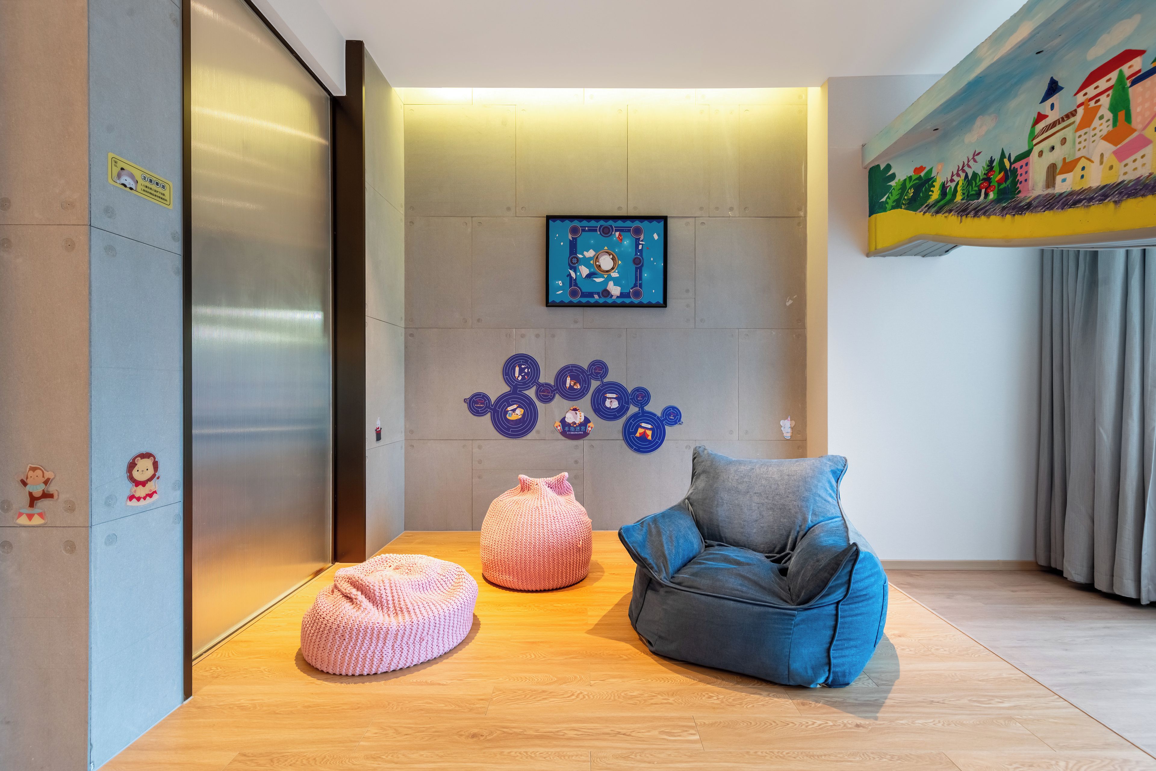 Un interior modern amb terra de fusta, una butaca de forma arrodonida blava, un otomana rosa i una paret amb decoracions circulars.