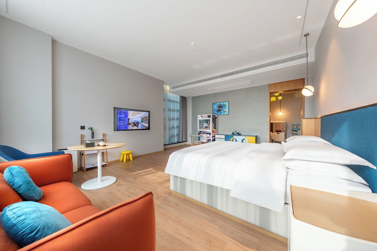 Habitació d'hotel moderna amb un llit gran, un sofà, una televisió i un escriptori.