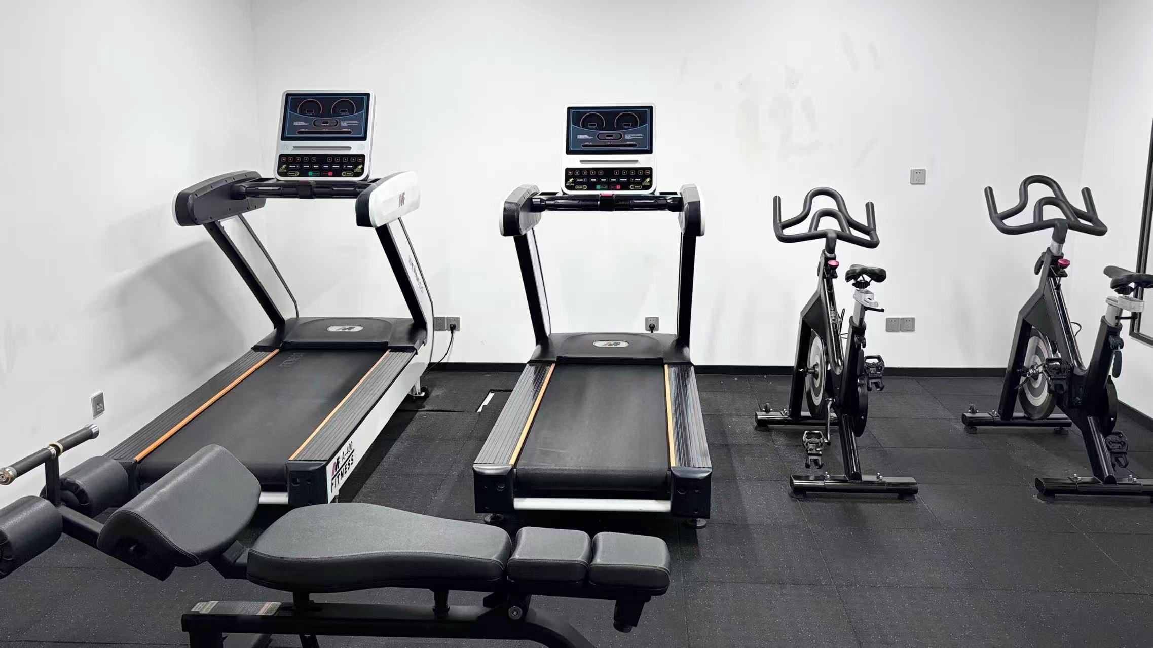 Un gimnasio con cintas de correr, bicicletas estáticas y bancos de pesas.