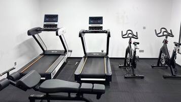 Un gimnasio con cintas de correr, bicicletas estáticas y bancos de pesas.