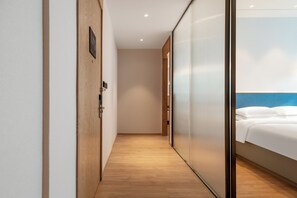 Un pasillo de hotel con piso de madera y una puerta corrediza que da a una habitación con cama y cabecera azul.