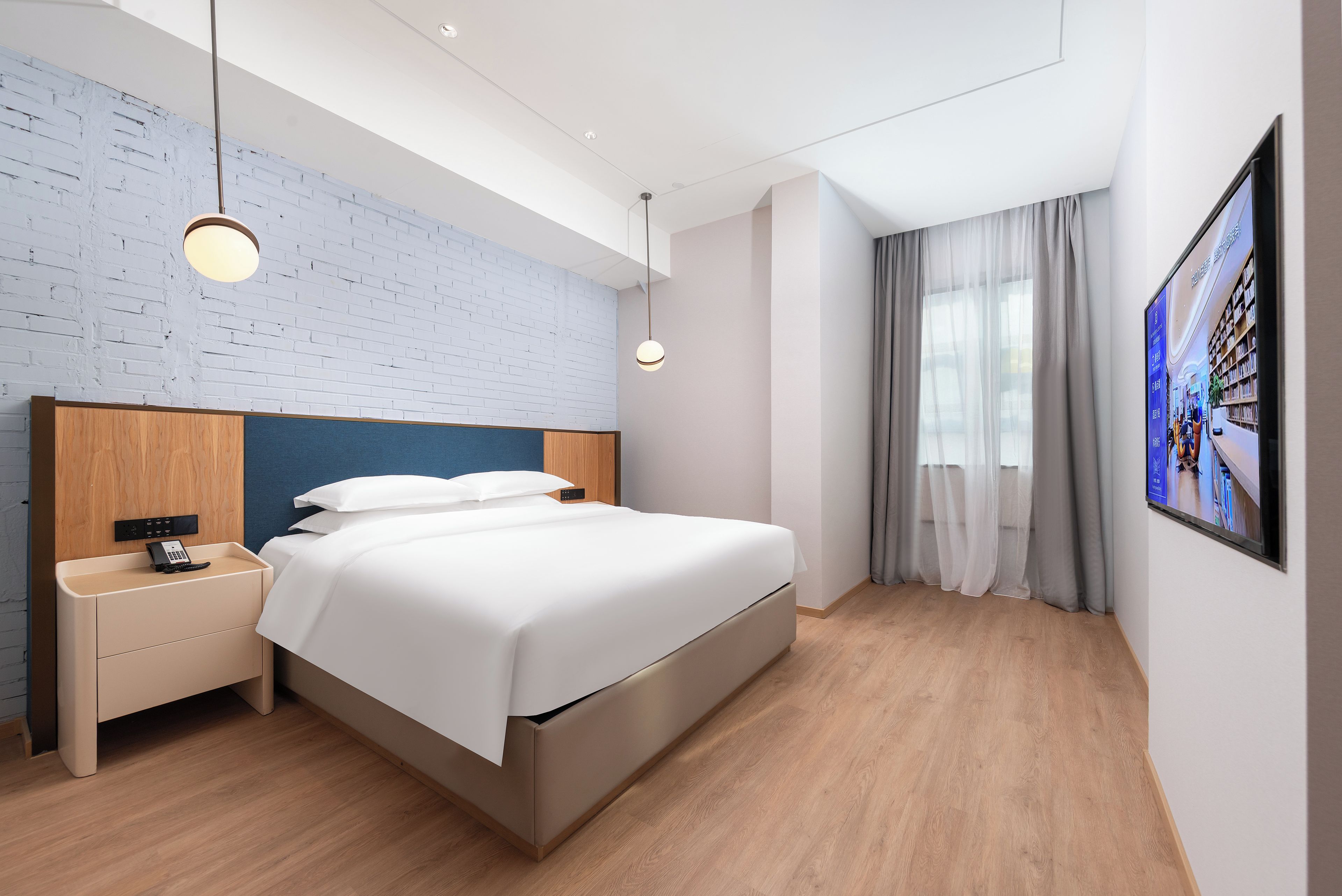 Una habitación de hotel moderna con una cama grande, mesitas de noche, un televisor en la pared y una pared con diseño de ladrillo.