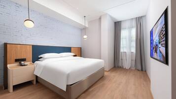 Una habitación de hotel moderna con una cama grande, mesitas de noche, un televisor en la pared y una pared con diseño de ladrillo.