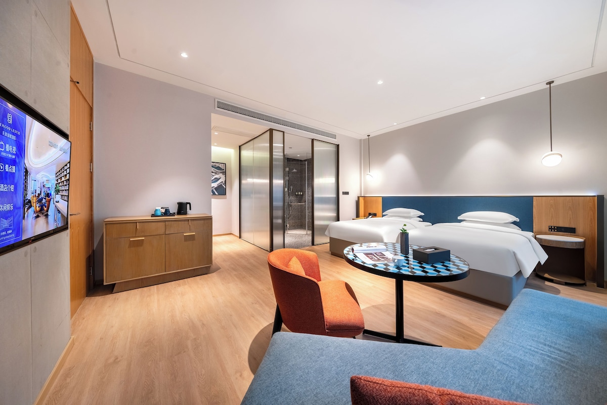 Habitació d'hotel moderna amb un llit, una taula de treball, una cadira i un televisor penjat a la paret.