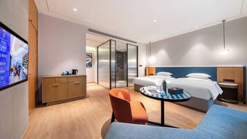 Una habitación de hotel moderna con cama, escritorio, silla y televisión en la pared.